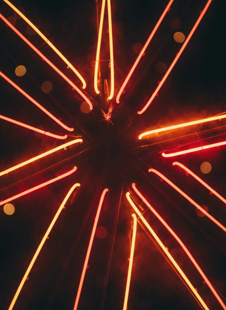 A dramatic neon lights background with vivid glowing neon tubes and streaks in electric red, orange, and yellow against a deep black background. Atmospheric bokeh and light diffusion, moody nightclub or concert venue aesthetic, no people, pure background only. Vertical portrait orientation.